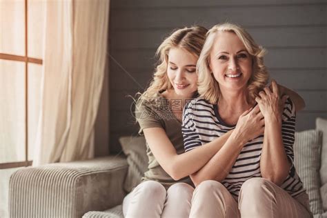 美丽的老妈和成年女儿在家中坐在沙发上时拥高清图片下载-正版图片503382420-摄图网