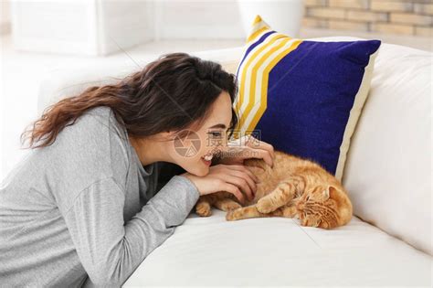 年轻女子和她的猫早上在家里闻到新鲜的粉红色郁金香的味道。高清摄影大图-千库网