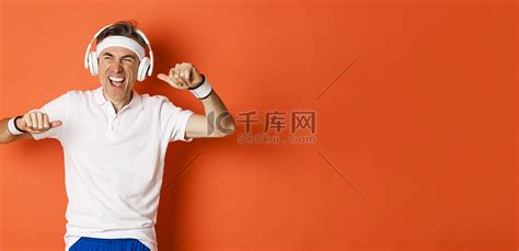 帅气的中年男运动员肖像，在健身训练中戴着耳机听音乐，在橙色背景下跳舞高清摄影大图-千库网