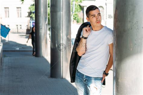 穿着白色T恤黑色皮夹克和蓝色破牛仔裤的年轻帅哥在街上高清图片下载-正版图片505766966-摄图网