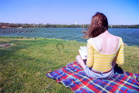 女孩坐在河边的草地上读着一本书高清图片下载-正版图片303490231-摄图网
