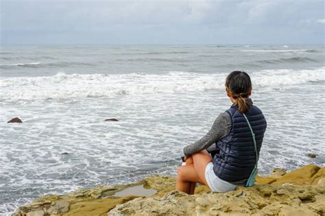年轻的亚洲女人坐在悬崖上，望着远方的大海。美丽的女孩在海滩上眺望大海。 令人振奋的时刻 一个年轻女子眺望地平线的画像正版图库-素材下载-图蜗创意图片库