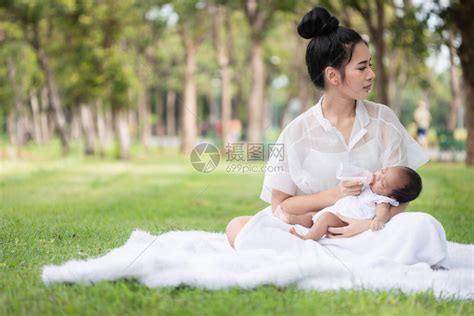 美丽的亚洲年轻母亲或带着新生女婴的单身母亲正在公园里用瓶子喂奶妻子和母亲在抚养孩子和家庭方高清图片下载-正版图片504380156-摄图网