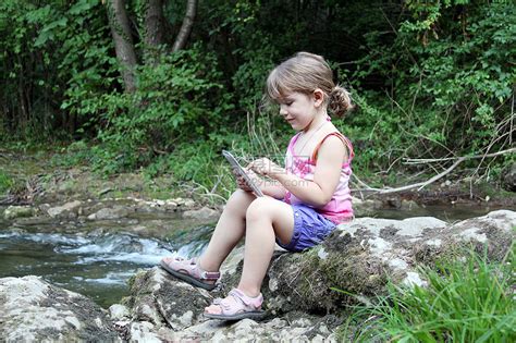 小女孩坐在溪边玩平板牌游戏的 小姑娘坐在河边高清图片下载-正版图片320767521-摄图网